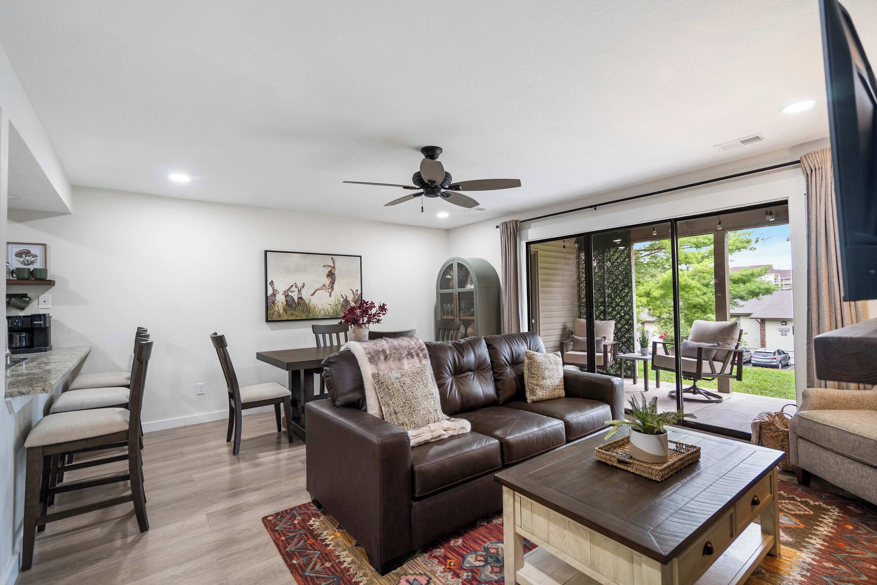 A modern living room with a brown leather sofa, a wooden coffee table, and a dining area with a table and chairs.