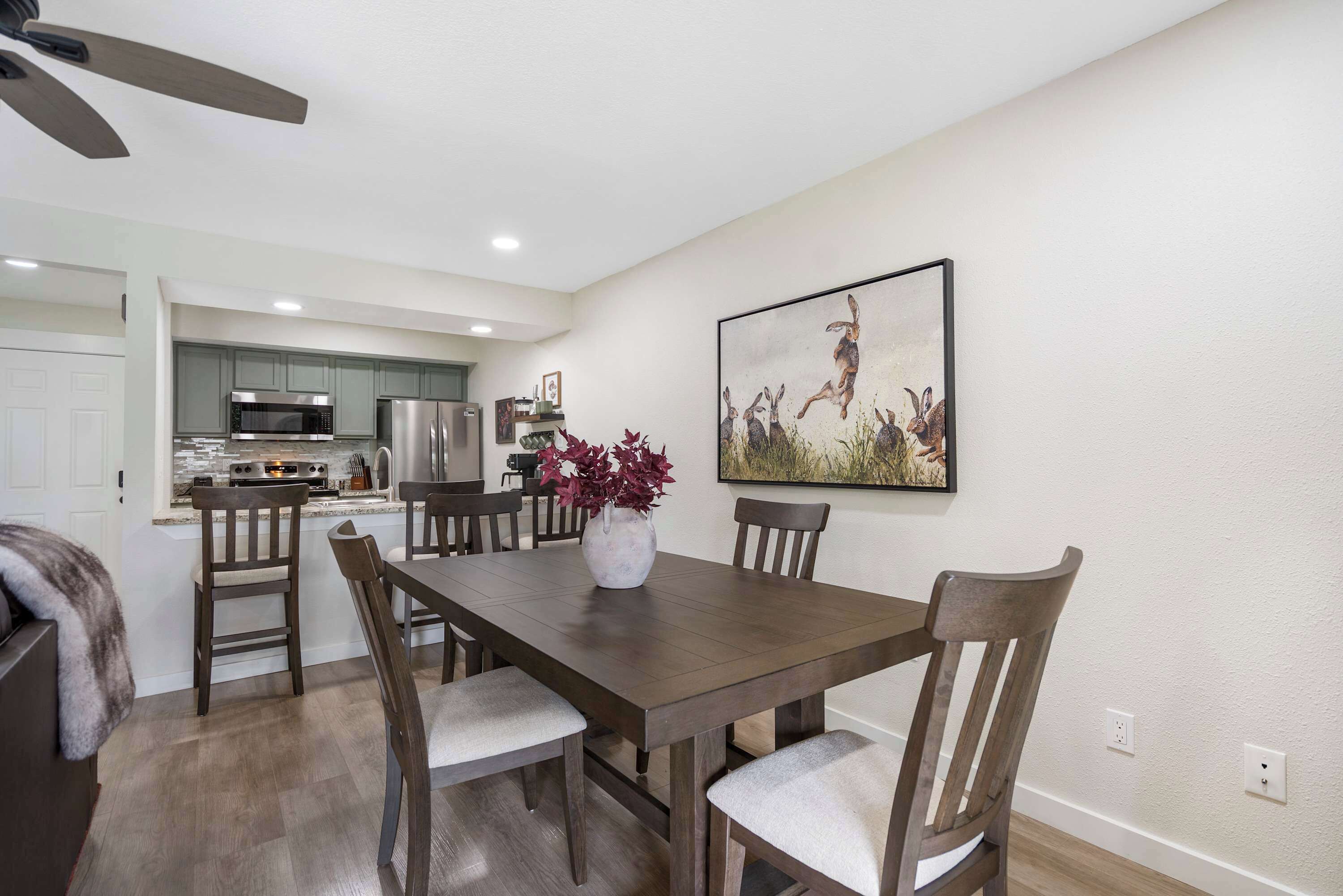 A dining area with a wooden table and chairs, a vase with flowers, and a painting on the wall.