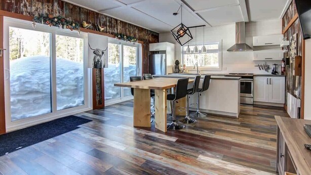 A modern kitchen with a central island, wooden flooring, and large windows with a snowy view.