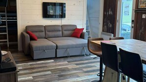 A modern living room with a grey sofa, a wooden dining table, and a bar stool.