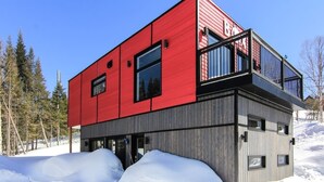 A modern two-story building with a red and grey exterior, large windows, and a balcony.