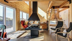 A modern cabin interior with a fireplace, wooden floors, and a staircase leading to an upper level.