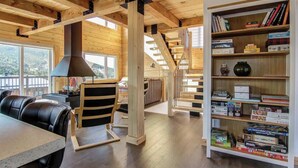 A spacious room with a wooden ceiling, a fireplace, a dining area with a table and chairs, and a bookshelf filled with books and board games.