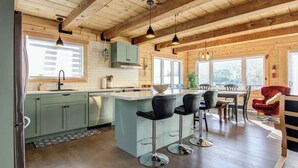 A modern kitchen with a central island, bar stools, and a dining area with a red chair.