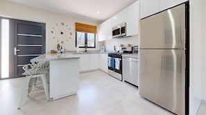 A modern kitchen with a central island, stainless steel appliances, and a large wall clock. - Palm Beach Hideaway #6: Poolfront 2BR/2BA, Rooftop, Near Palm Beach (Noord)