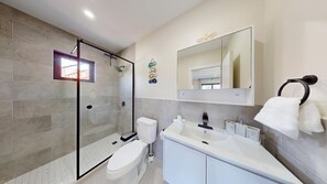 Ein modernes Badezimmer mit einer gläsernen Duschkabine, einer Toilette, einem Waschbecken und einem großen Spiegel.