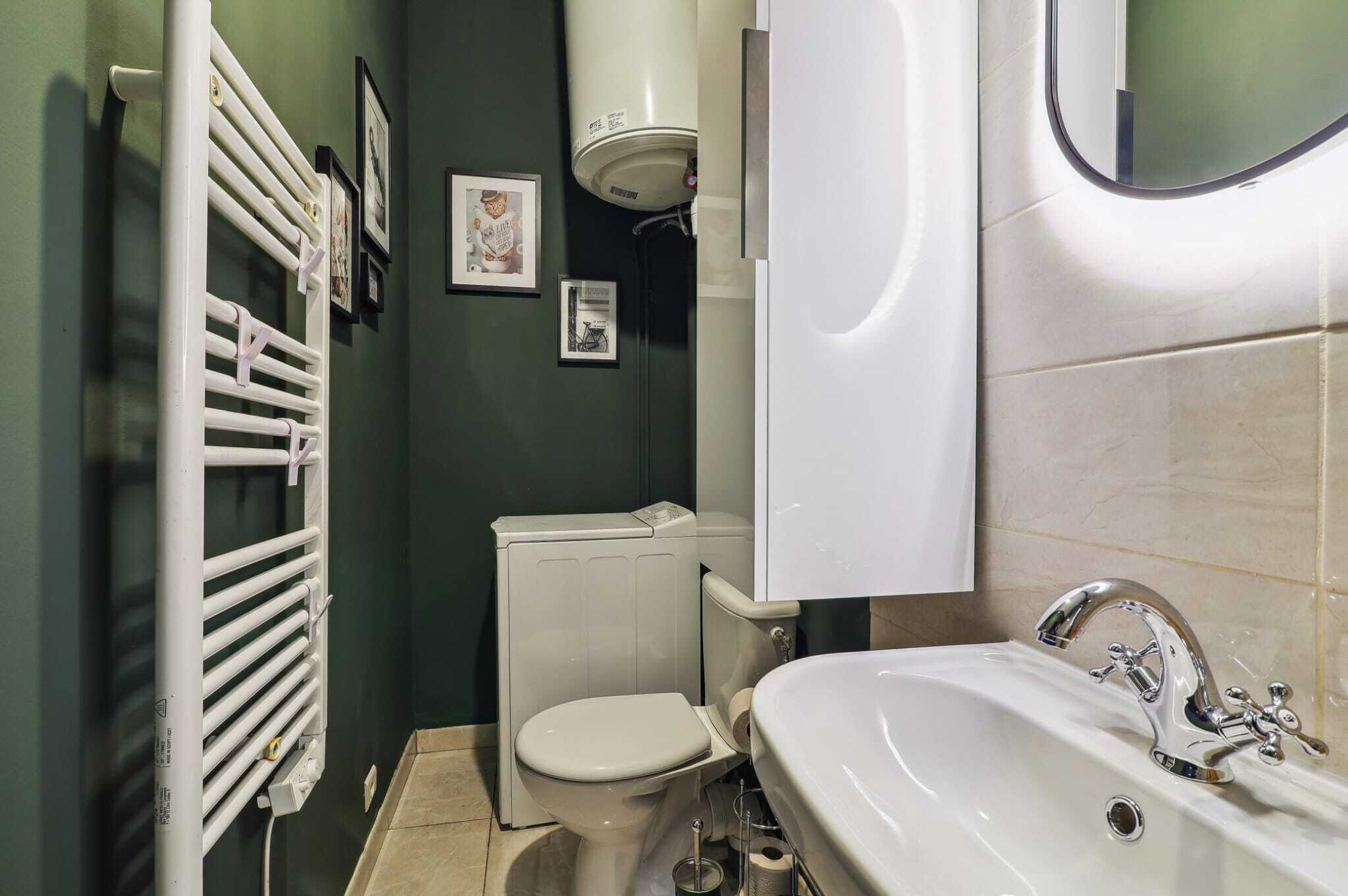 Een badkamer met een witte radiator, toilet, wastafel en een spiegel.