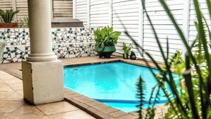 A swimming pool with tiled flooring and potted plants.