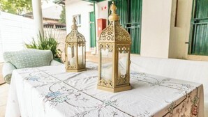 Two ornate lanterns on a table with a floral tablecloth, set outdoors with a building in the background.