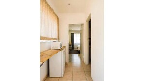 A narrow hallway with a kitchen area on the left, featuring a microwave and a refrigerator. The hallway leads to a door at the end.