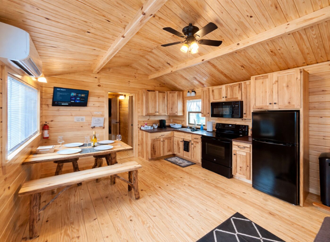 Interno di una baita in legno con tavolo da pranzo, angolo cottura e ventilatore a soffitto.