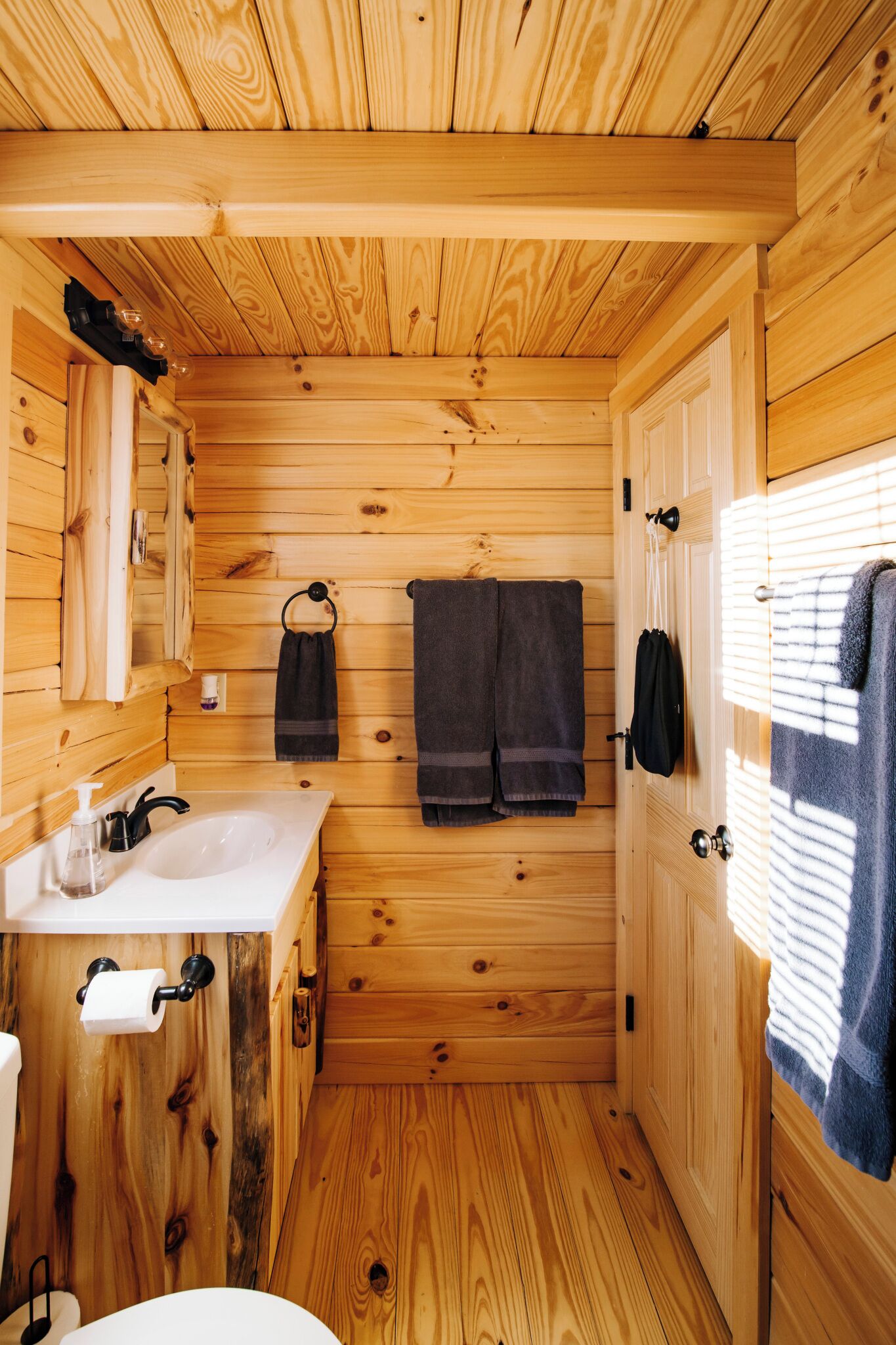 Un baño de cabaña de madera con lavamanos, toallero y armarios de madera.