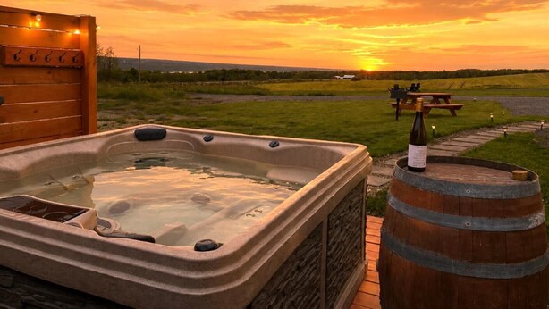 A hot tub with a wooden bench and a barrel, set against a sunset view. - Cozy Cabin • Hot Tub • Wineries • Sunset Views 6 (Hector)