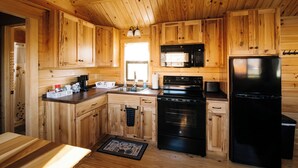 A wooden cabin interior with a kitchen featuring wooden cabinets, a black stove, a refrigerator, and a coffee bar. - Cozy Cabin • Hot Tub • Wineries • Sunset Views 6 (Hector)