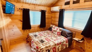 A cozy wooden cabin room with a bed, a ceiling fan, and a mounted TV. - Cozy Cabin • Hot Tub • Wineries • Sunset Views 6 (Hector)