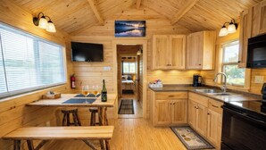 A wooden interior with a dining table, benches, a kitchen area, and a TV mounted on the wall. - Cozy Cabin • Hot Tub • Wineries • Sunset Views 6 (Hector)