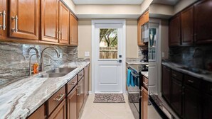 A kitchen with wooden cabinets, a marble countertop, a sink, and a door leading to another room. - 2BR - Hot Tub W/ Peaceful Backyard • 1 Mi to Beach (Boca Raton)