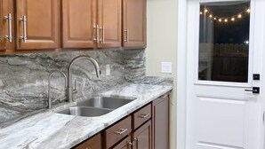 A kitchen with marble countertops, a double sink, wooden cabinets, and a white door with a window. - 2BR - Hot Tub W/ Peaceful Backyard • 1 Mi to Beach (Boca Raton)