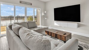 Un salon moderne avec un grand canapé d’angle, une table basse en bois et un téléviseur fixé au mur.