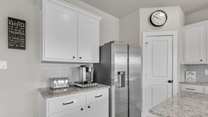 Une cuisine moderne avec des meubles blancs, un réfrigérateur en acier inoxydable, une machine à café et une horloge murale.