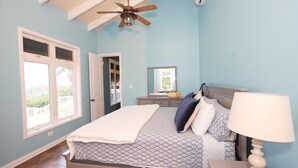 A bedroom with a bed, a nightstand, a lamp, a ceiling fan, and a window. - Almost Heaven: 5 Bed Villa (Christiansted)