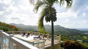 Un balcon avec des fauteuils de jardin, un palmier et une vue sur les montagnes et la verdure.
