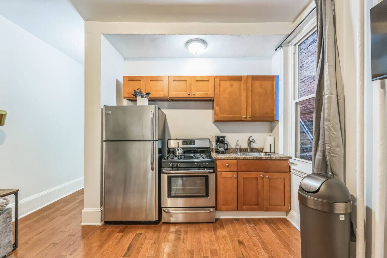 Una cocina compacta con armarios de madera, un refrigerador de acero inoxidable, una estufa y un horno.