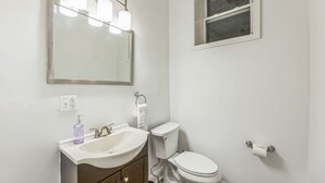 Ein Badezimmer mit einem weißen Waschbecken, einem beleuchteten Spiegel, einer Toilette und einem Fenster.