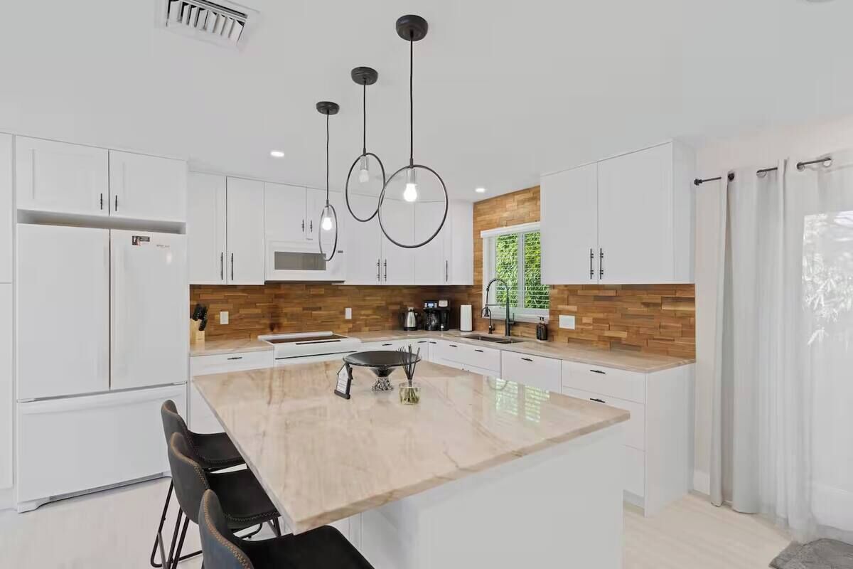 Una cucina moderna con mobili bianchi, un'isola centrale e illuminazione a sospensione.