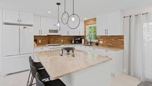 Una cocina moderna con armarios blancos, una isla central e iluminación colgante.