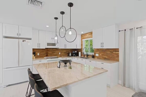 A modern kitchen with white cabinets, a central island, and pendant lighting.