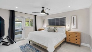 Un dormitorio con cama, mesitas de noche, ventilador de techo y ventana con persianas.
