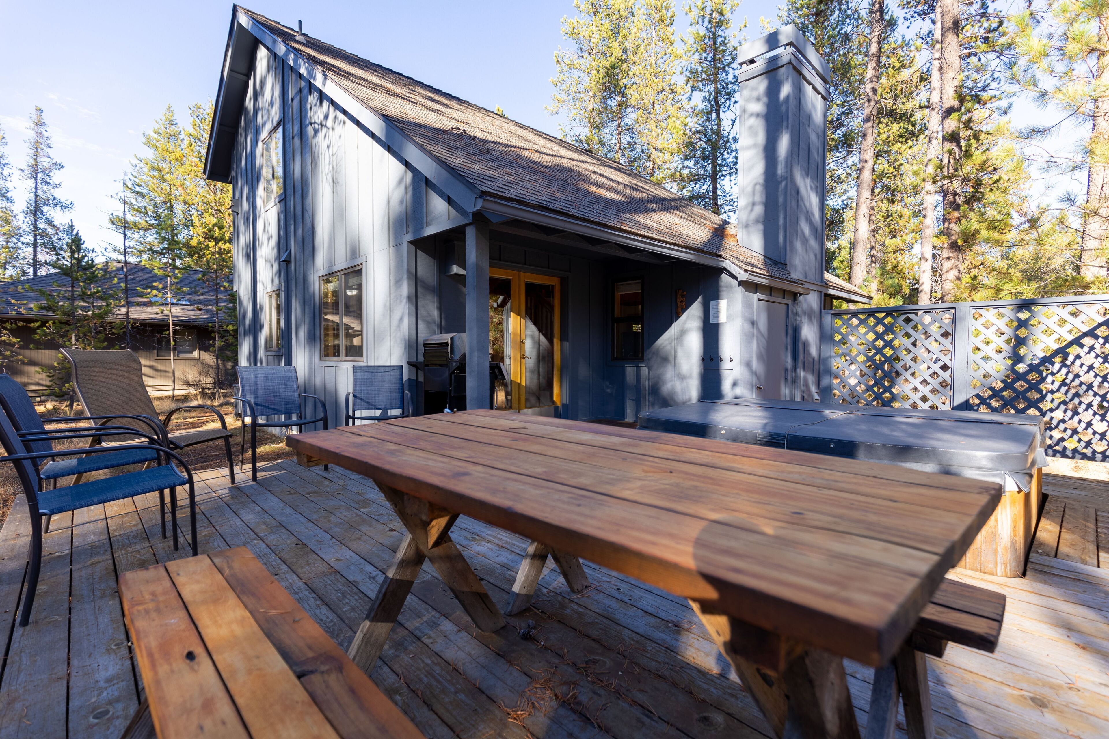 A wooden deck with a table and chairs, a covered outdoor area, and a building with a chimney.