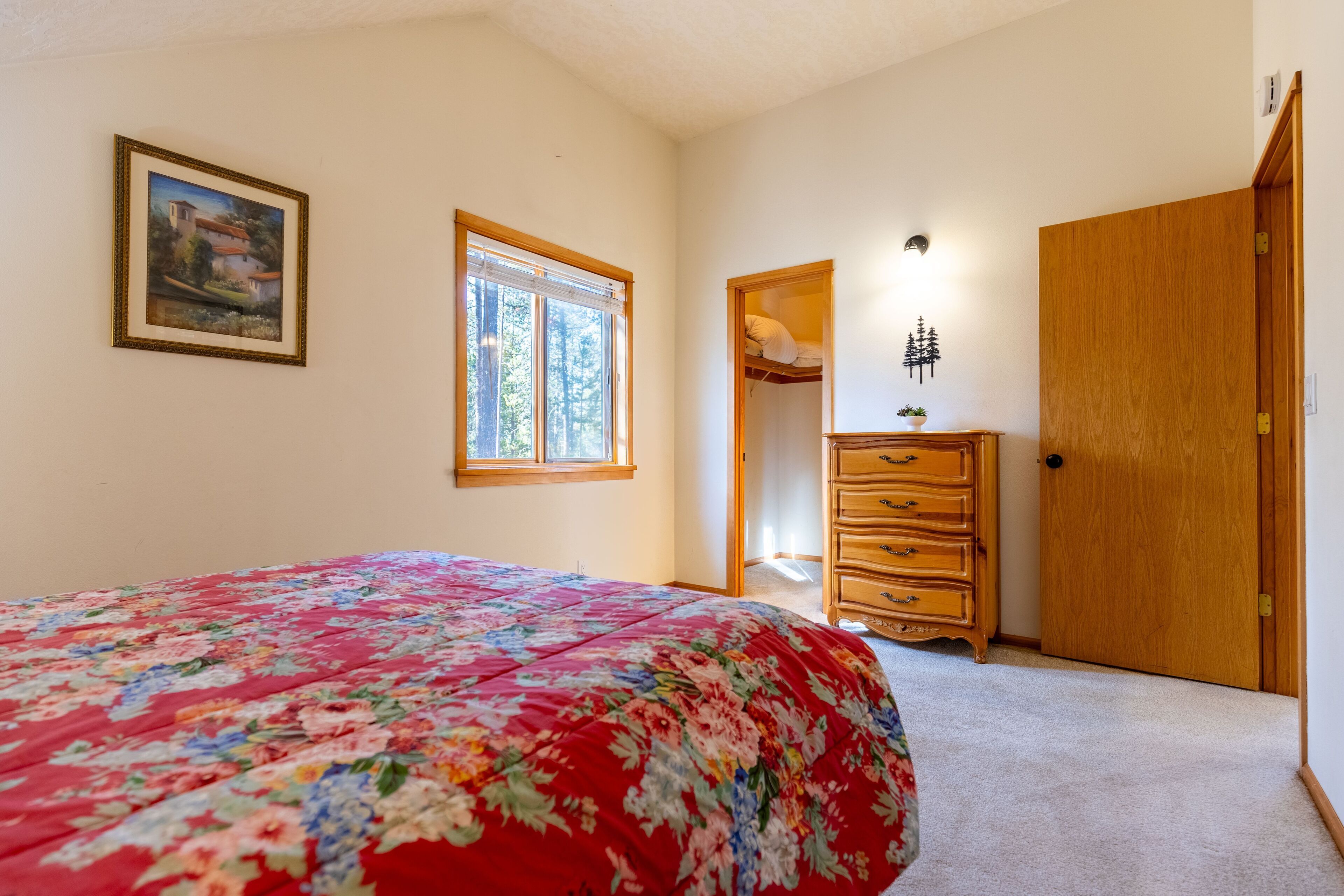A bedroom with a floral bedspread, a window, a dresser, and a door.
