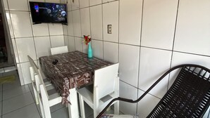 A small dining area with a table and chairs, a flat-screen TV mounted on the wall, and a vase with flowers on the table. - Apartment in Coroado, Manaus, close to buses, restaurants and markets. (Manaus)