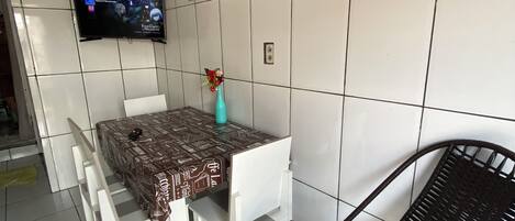Et lille spiseområde med et bord og stole, et vægmonteret fladskærms-tv og en vase med blomster på bordet.