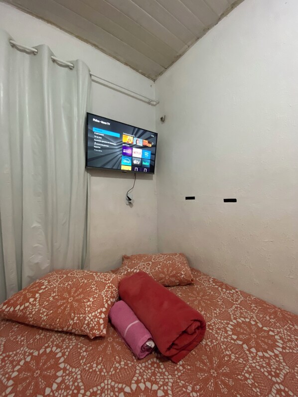 Una habitación pequeña con una cama, un televisor en la pared y una cortina.