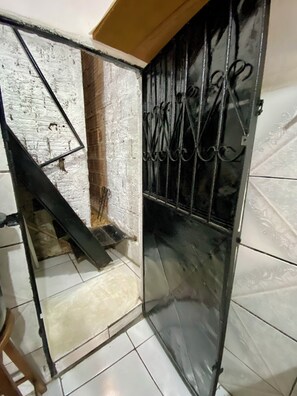 Una habitación con una escalera que baja a un nivel inferior, una reja metálica con barandales decorativos y suelo de baldosas.