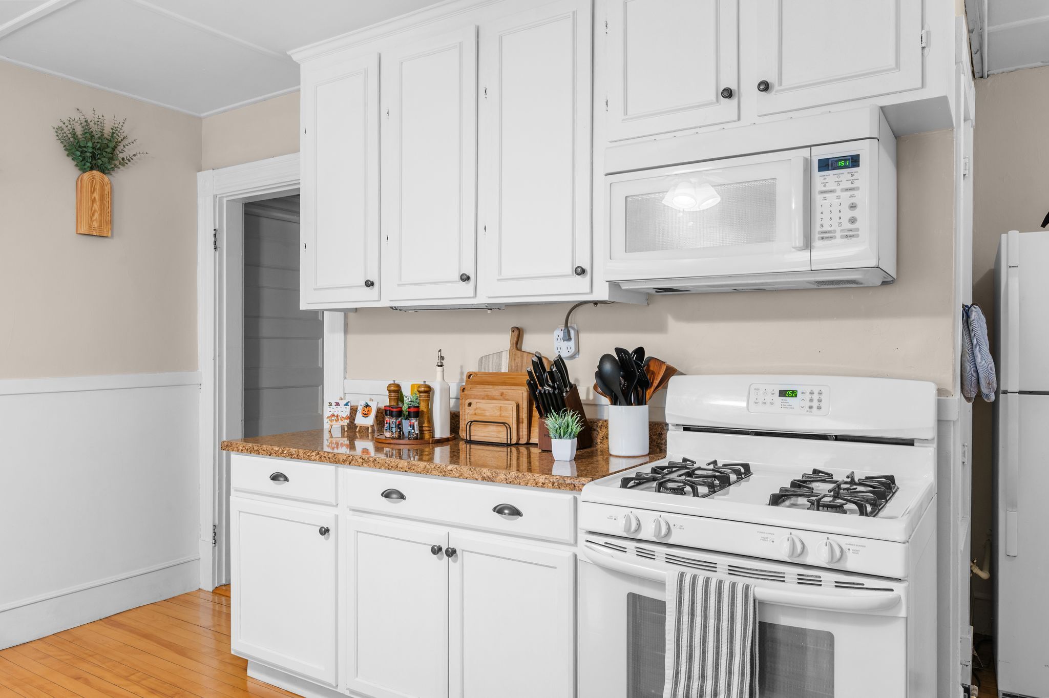 Una cocina con gabinetes blancos, microondas, estufa y diversos utensilios de cocina sobre la encimera.