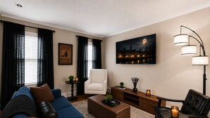 A modern living room with a blue sofa, a white armchair, a wooden coffee table, and a floor lamp. - The Witch City Hideout - Salem 3 Bedroom with Gameroom, Balcony & Free Parking (Salem)