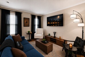A modern living room with a blue sofa, a white armchair, a wooden coffee table, and a floor lamp. - The Witch City Hideout - Salem 3 Bedroom with Gameroom, Balcony & Free Parking (Salem)