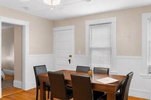 A dining room with a wooden table and chairs, a door, and a window with blinds. - The Witch City Hideout - Salem 3 Bedroom with Gameroom, Balcony & Free Parking (Salem)