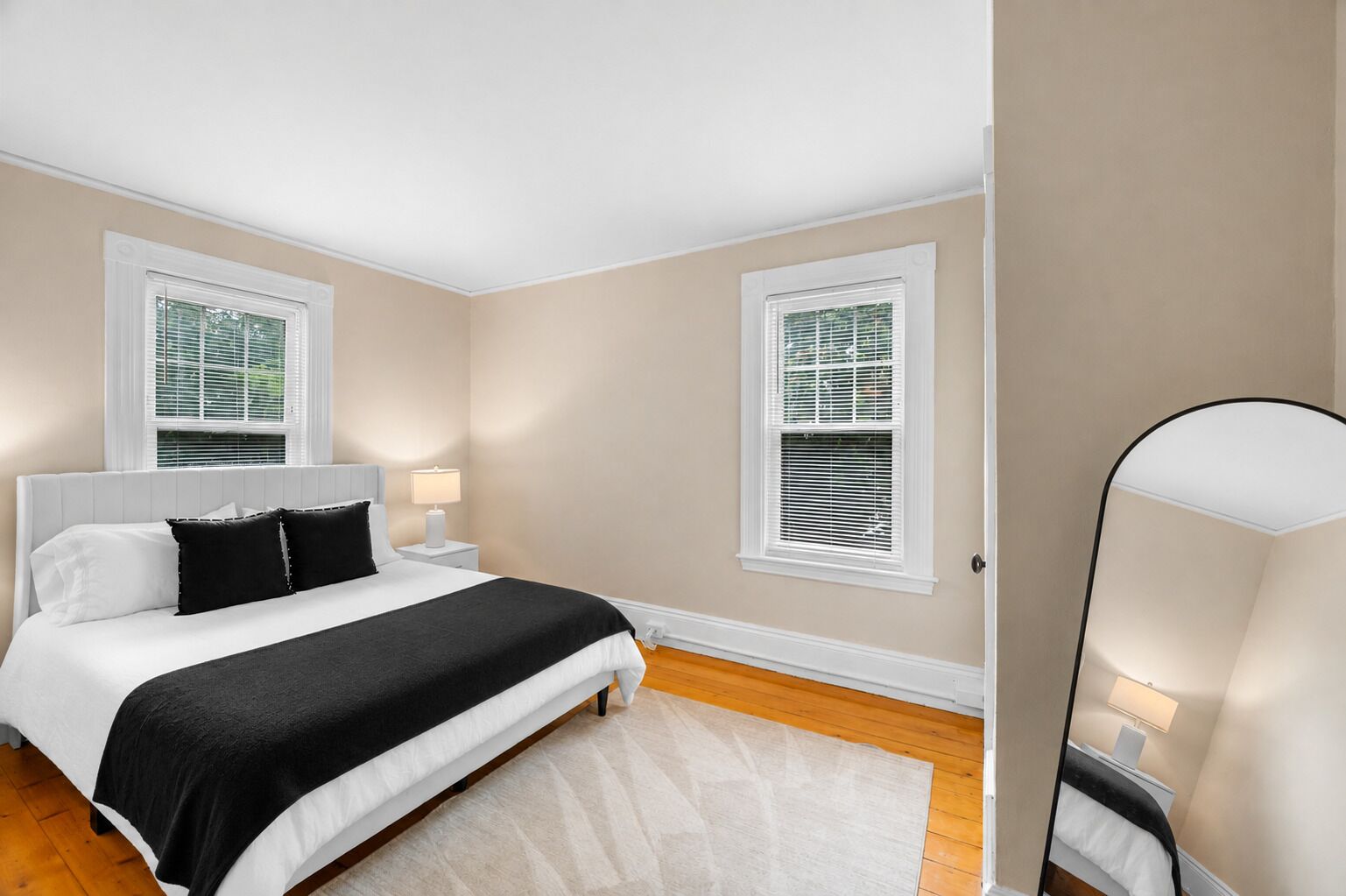 A bedroom with a bed, bedside tables, a nightstand, and two windows with blinds.