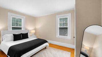 A bedroom with a bed, bedside tables, a nightstand, and two windows with blinds.