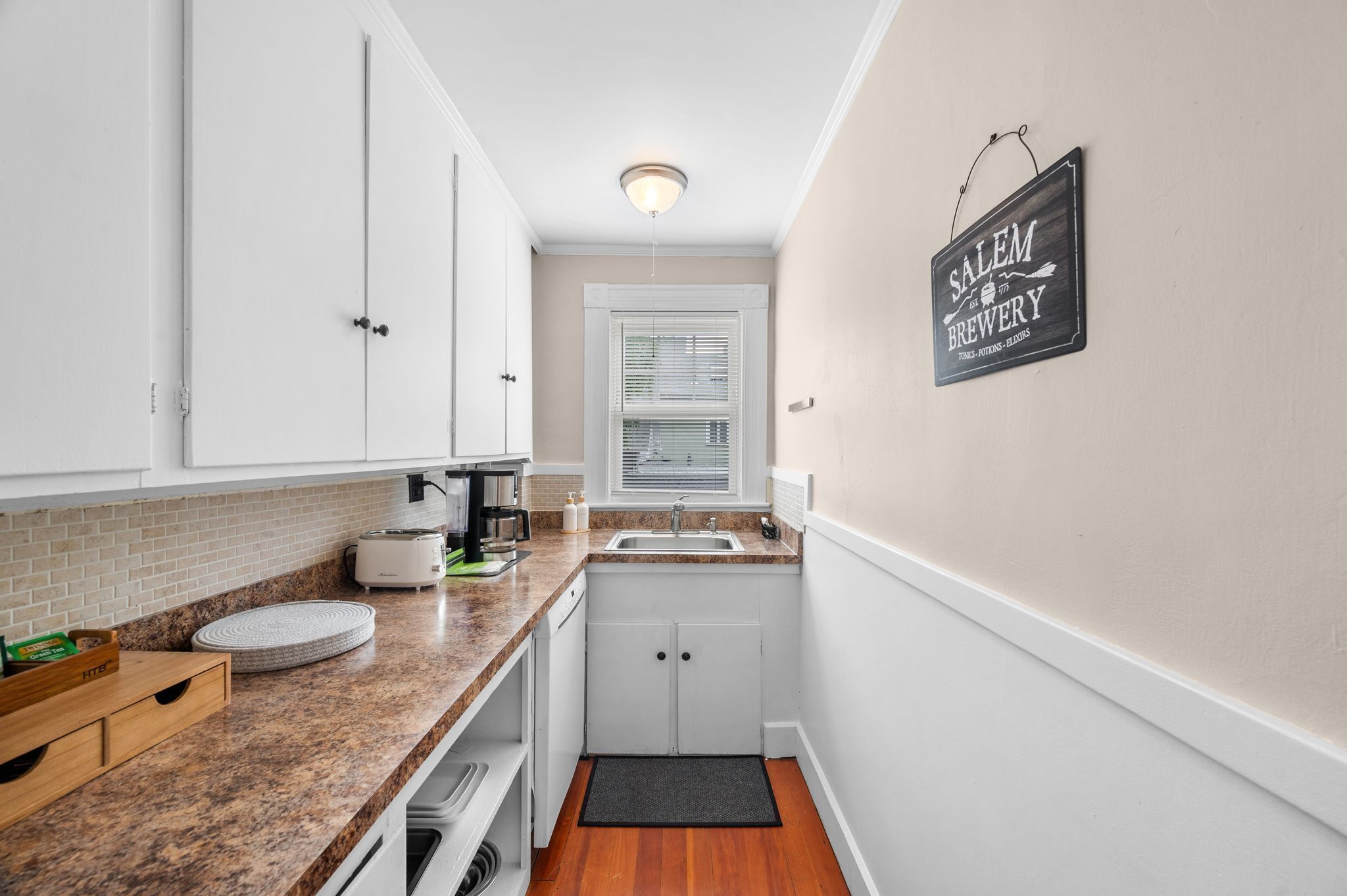 A compact kitchen with white cabinets, a granite countertop, a coffee maker, and a sign on the wall.