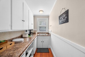A compact kitchen with white cabinets, a granite countertop, a coffee maker, and a sign on the wall. - The Witch City Hideout - Salem 3 Bedroom with Gameroom, Balcony & Free Parking (Salem)