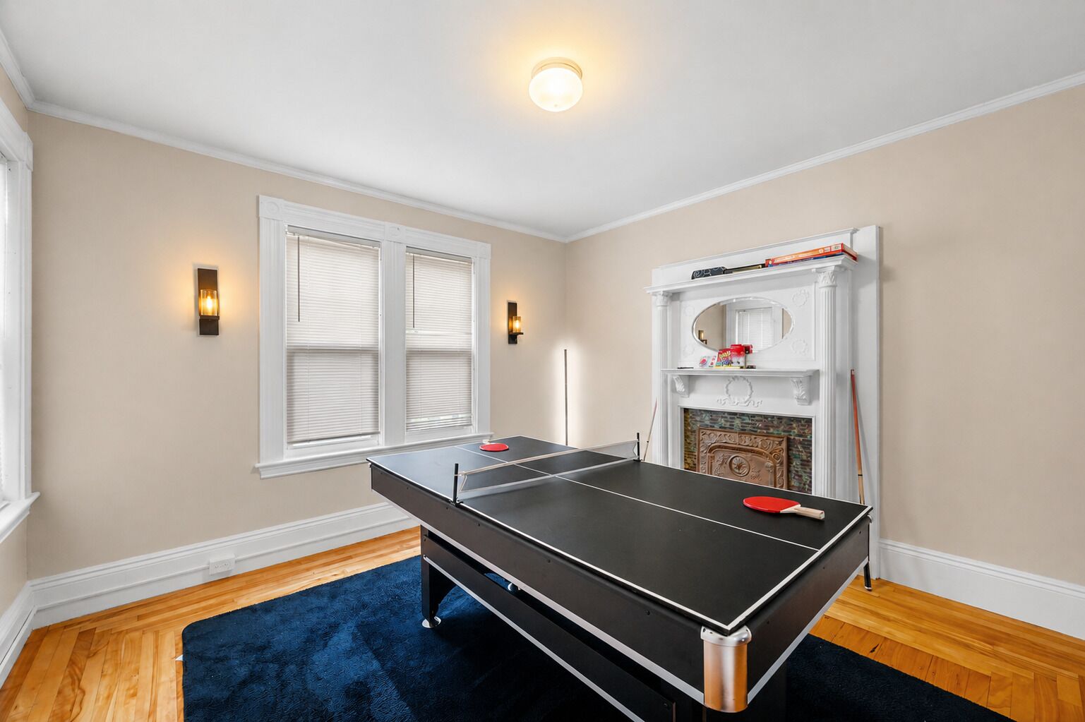 A room with a ping pong table, a fireplace, and two wall-mounted lights.