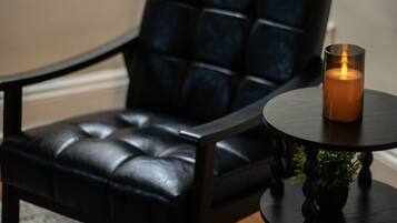 A black leather chair with a cushion, a small round table with a candle, and a patterned rug.