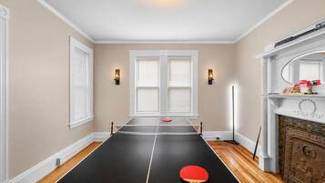 A room with a ping pong table, two wall-mounted lights, a fireplace, and a mirror above it.