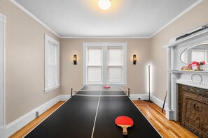 A room with a ping pong table, two wall-mounted lights, a fireplace, and a mirror above it. - The Witch City Hideout - Salem 3 Bedroom with Gameroom, Balcony & Free Parking (Salem)